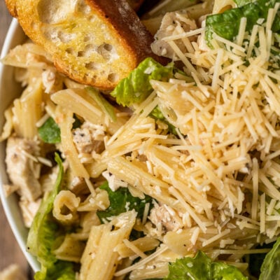 A bowl of chicken ceasar pasta salad topped with parmesean cheese near grilled bread